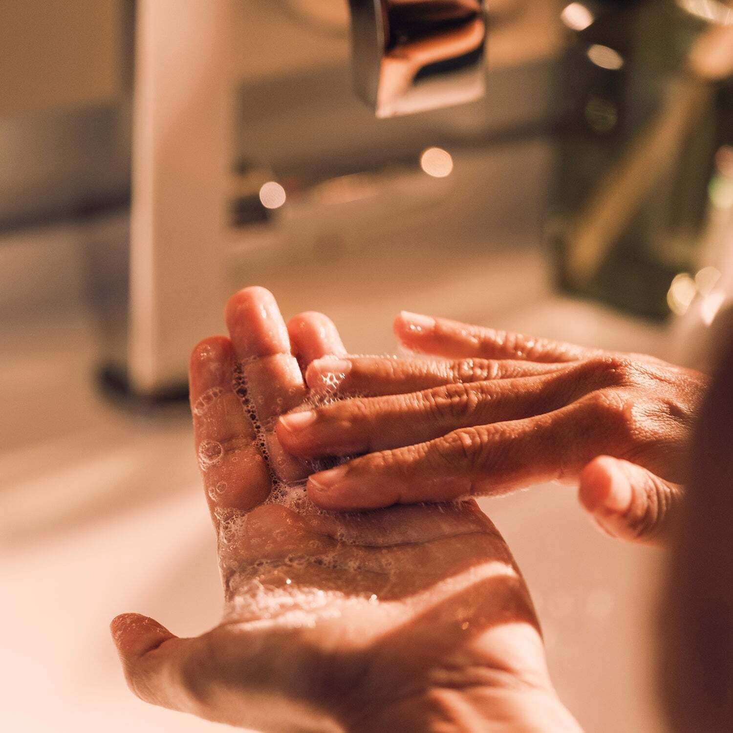 Hände mit Seifenschaum. Hintergrund: Waschbecken und Wasserhahn.