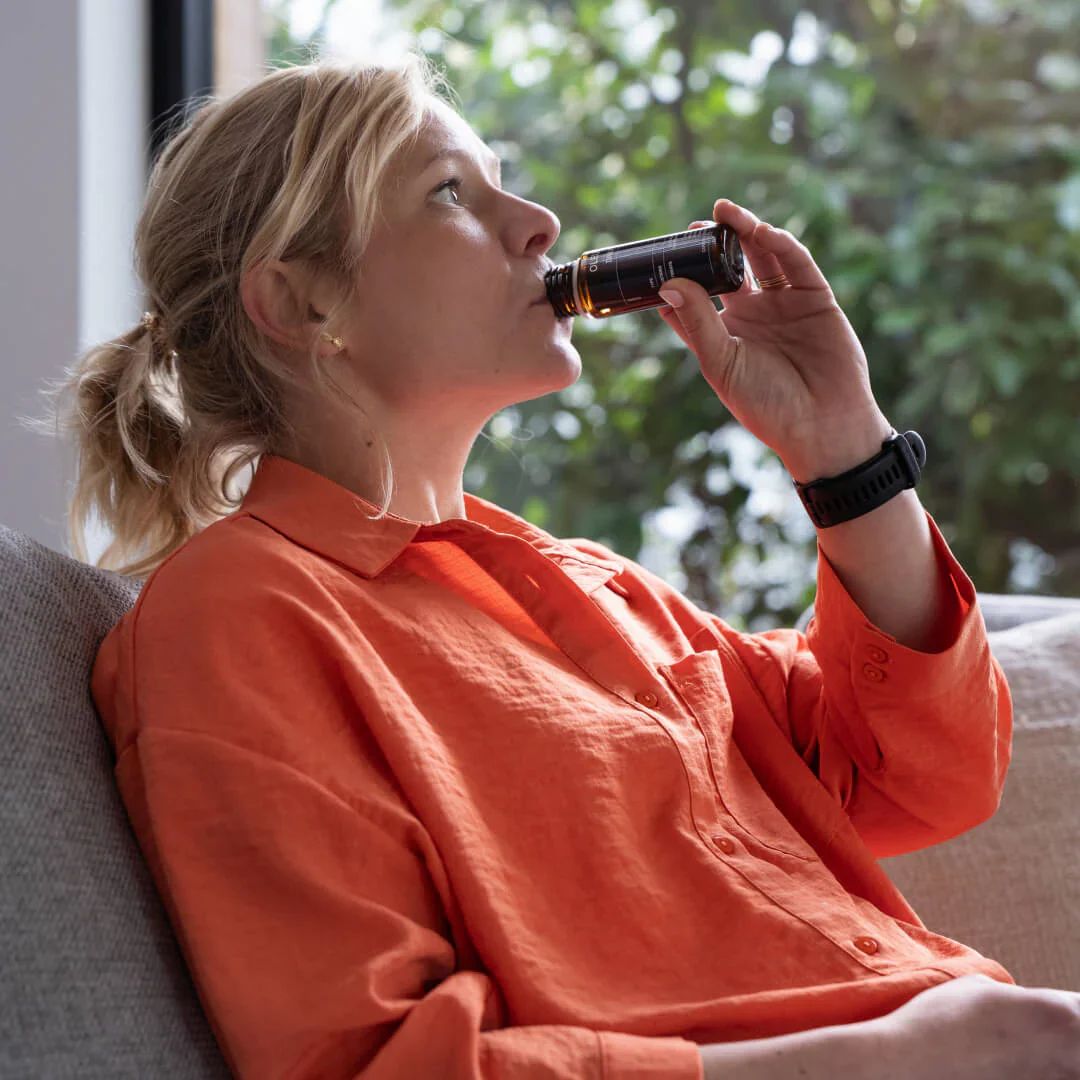 Frau trinkt aus Flasche. OLEUS-Logo und Produktetikett sichtbar. Schwarze Flasche.