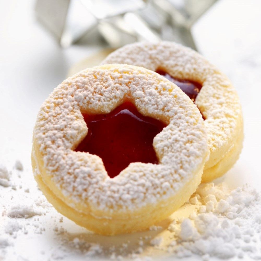 Zwei Weihnachtsplätzchen mit roter Füllung und Puderzucker. Sternförmige Aussparung. Auf weißem Untergrund.