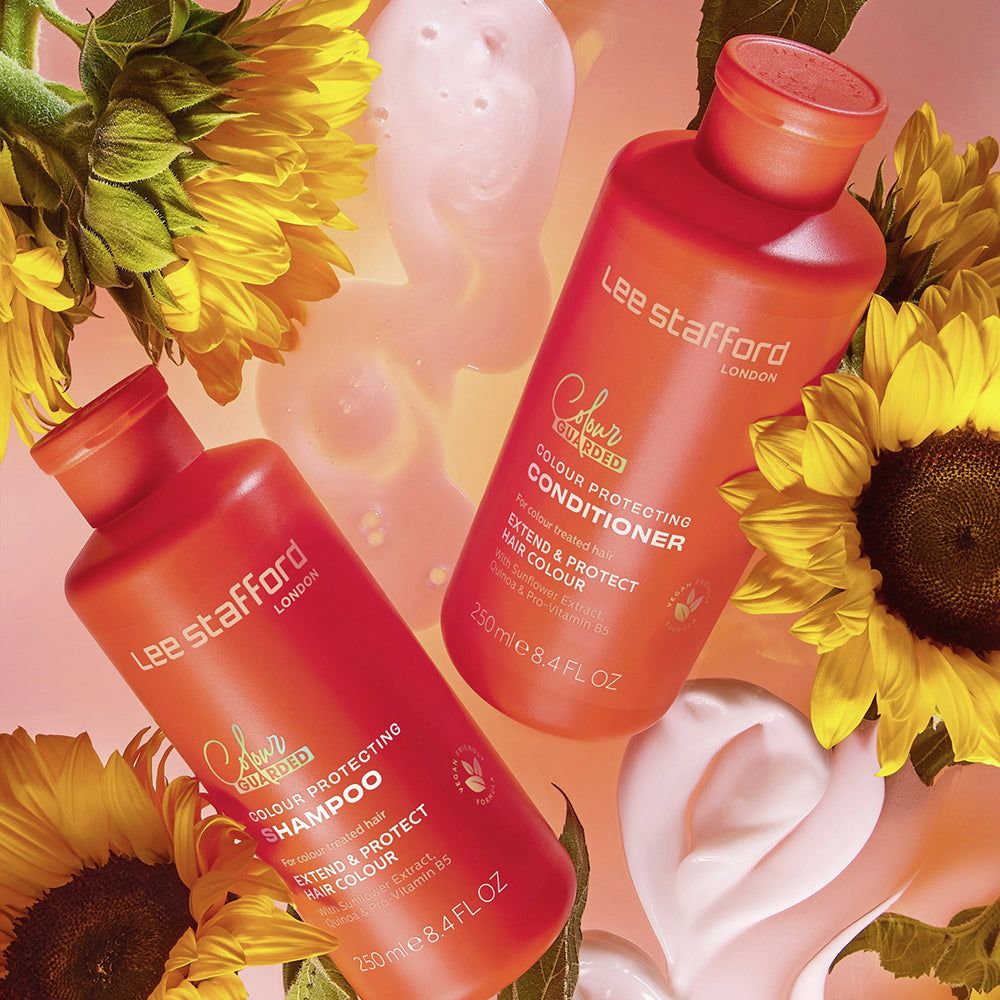 Zwei orangefarbene Flaschen, Lee Stafford Conditioner und Shampoo, mit Sonnenblumen und cremigen Elementen.