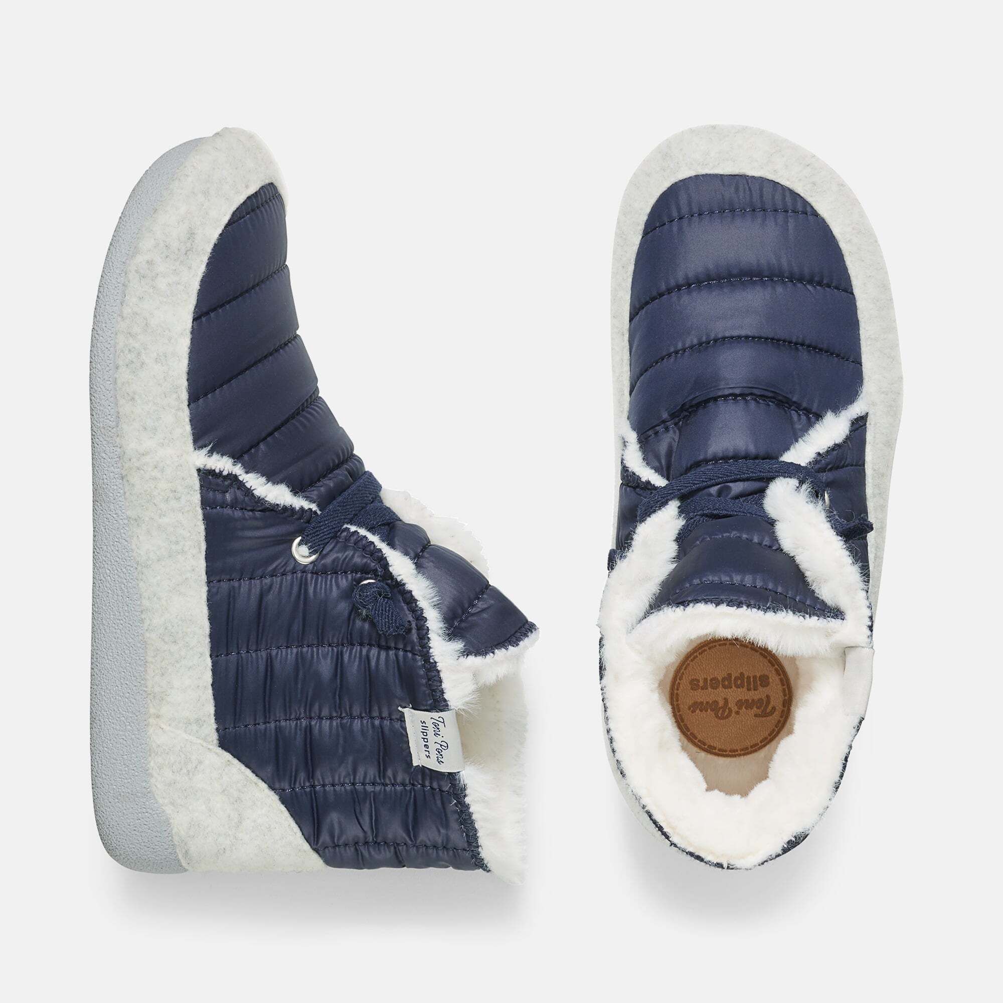 Draufsicht auf blaue Pantoletten/Hausschuhe. Weißes Fellfutter, Schnürsenkel. Innen Sohle mit Aufdruck.