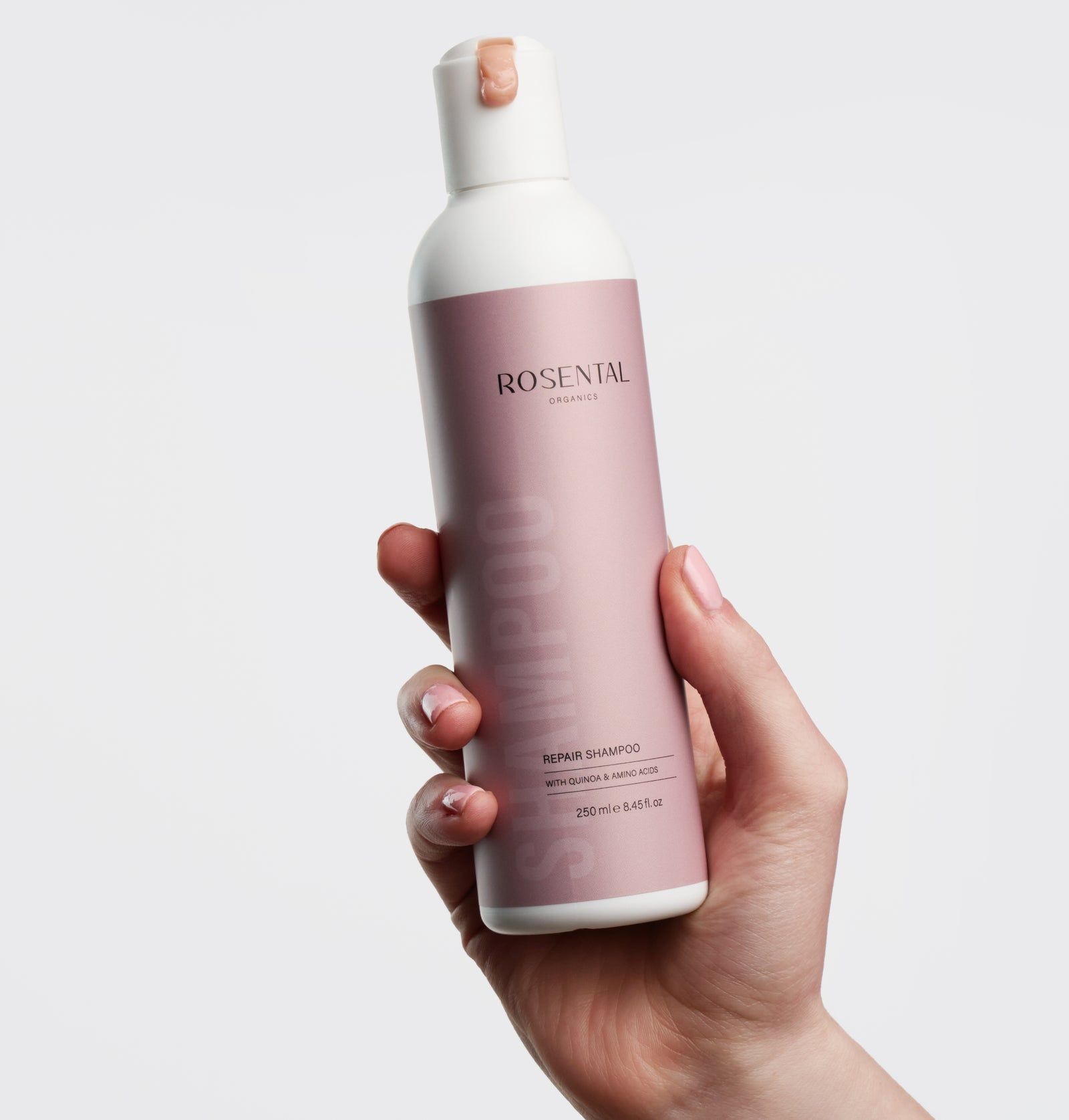 Eine Hand hält eine rosa Shampoo-Flasche. Auf der Flasche steht "Rosental Organics Repair Shampoo".
