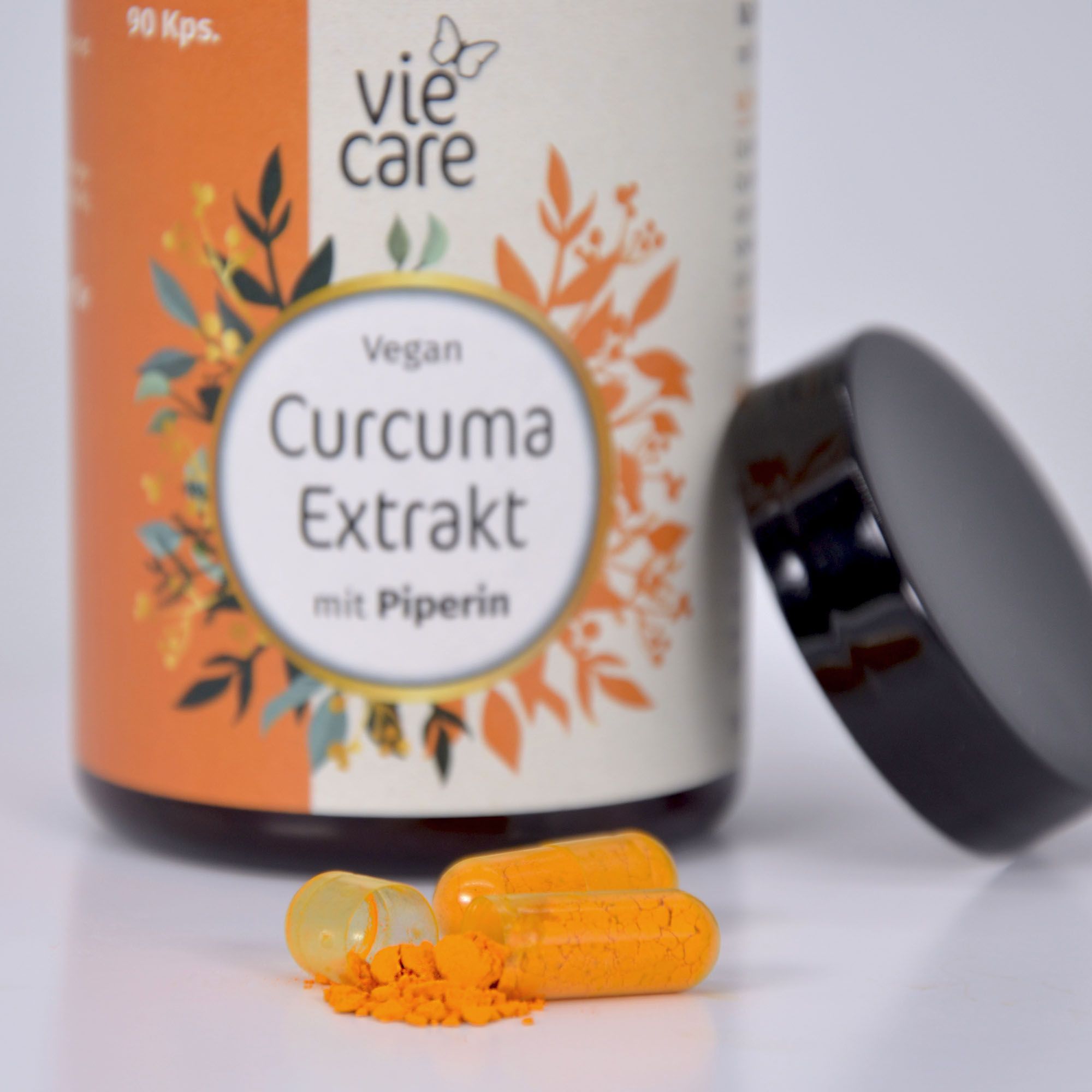 Braune Kapseln und Pulver neben geöffneter Flasche. Etikett mit "vie care" und "Curcuma Extrakt mit Piperin".