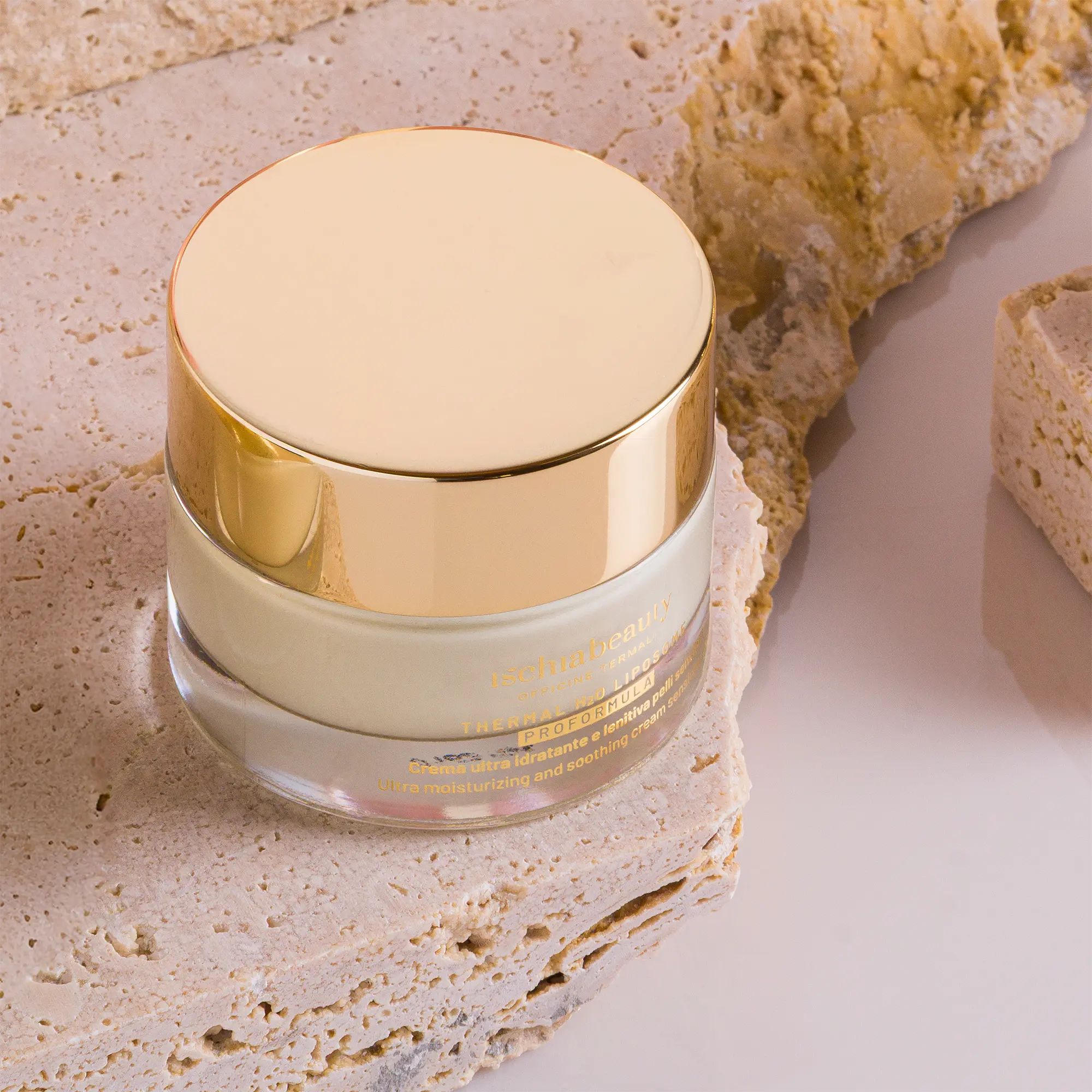Creme-Behälter mit goldenem Deckel. Auf Stein platziert. Text: ischiabeauty, Thermal H2O Liposome, Proformula.