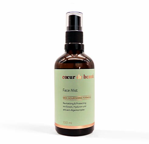 Braune Glasflasche mit Zerstäuber. Aufschrift: Coeur de Beauté, Face Mist, Skin Nourishing Formula. Etikett mit Text in Deutsch.