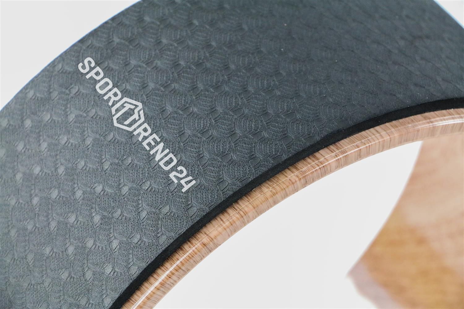 Nahaufnahme eines Yoga-Rads. Schwarze, strukturierte Oberfläche mit Aufschrift Sporttrend24. Holzoptik.
