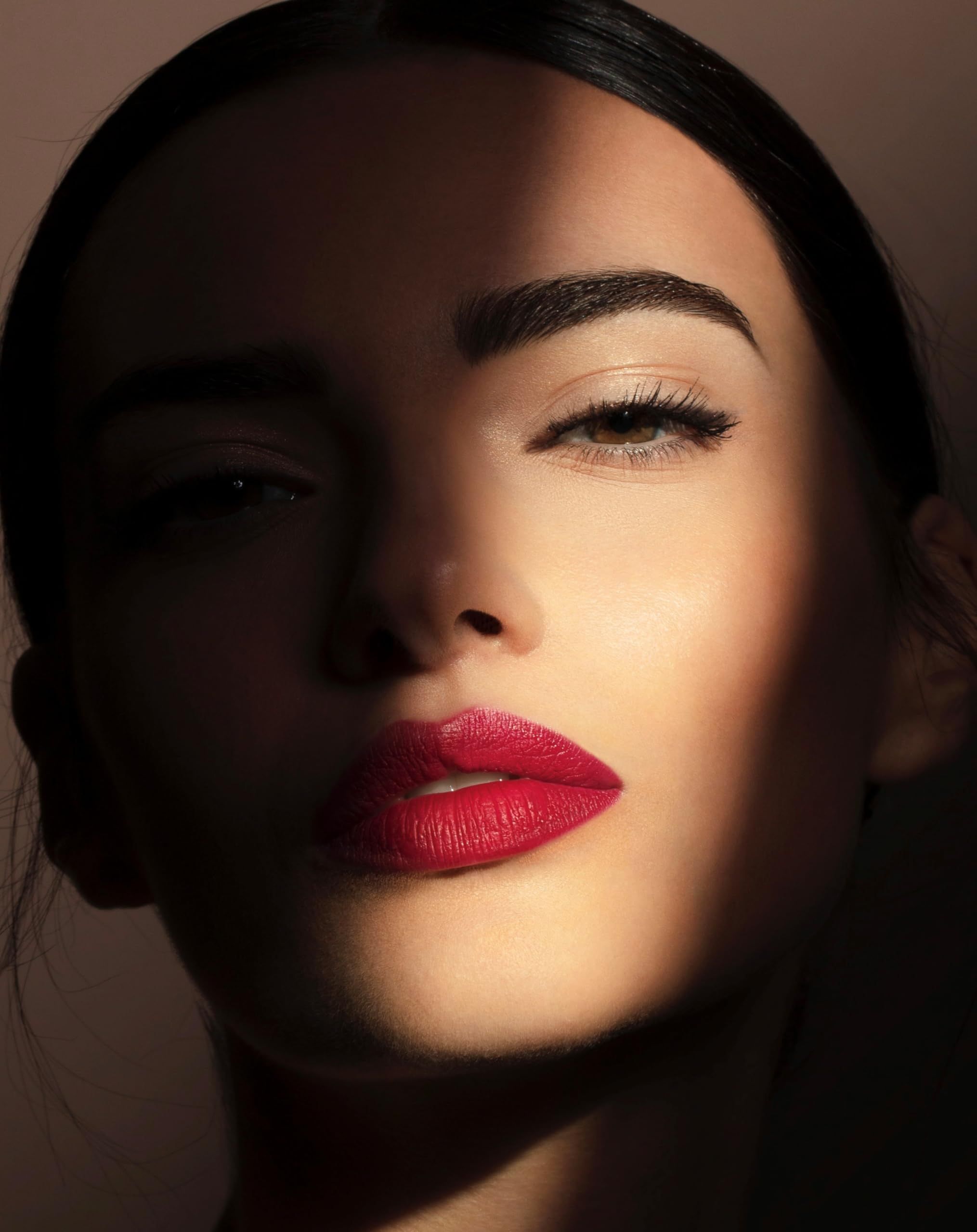 Porträt einer Frau mit rotem Lippenstift, das Gesicht zur Hälfte im Schatten.