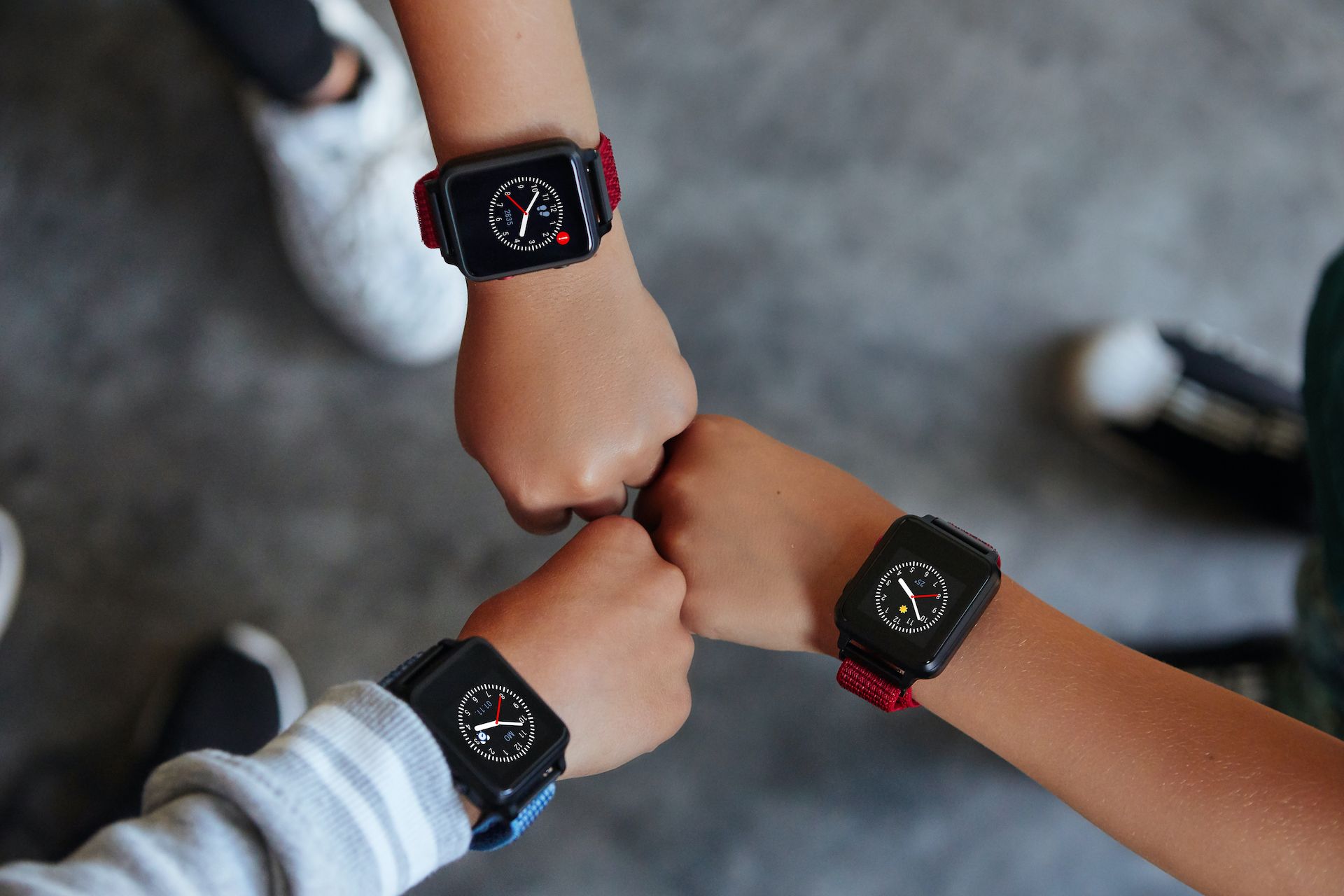Drei Kinderarme mit Smartwatches. Schwarze Uhren mit farbigen Armbändern. Hände zusammen.