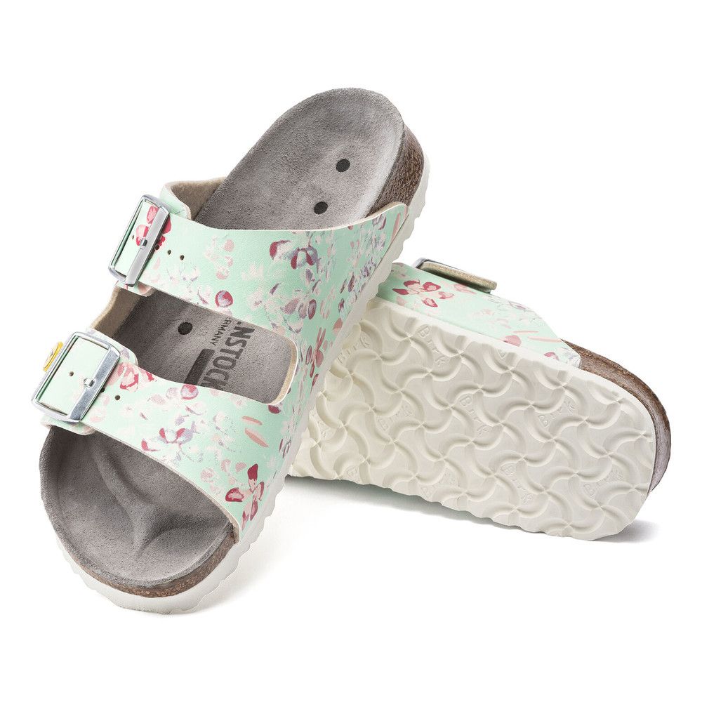 Türkis-farbene Sandalen mit Blumenmuster, zwei Riemen mit Schnallen, Korkfußbett, eine Sandale liegt.