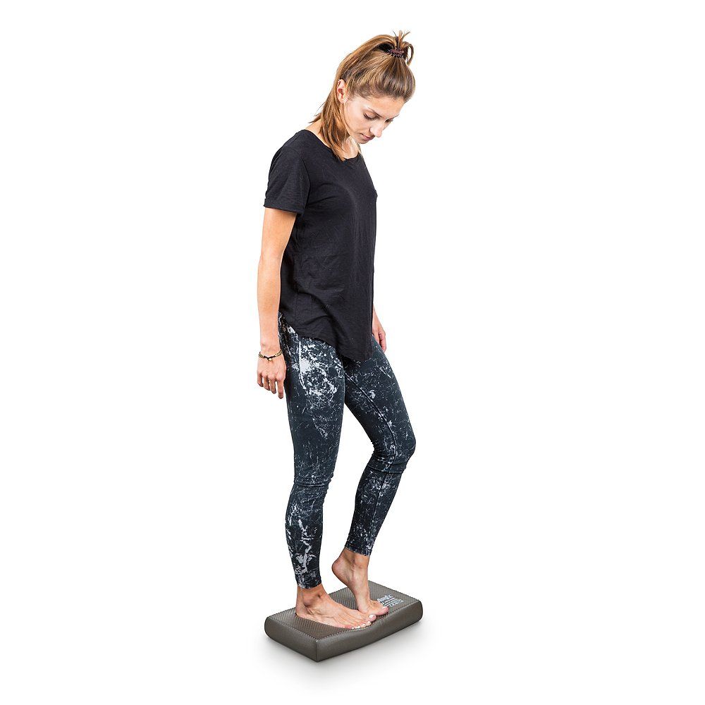 Eine Frau steht auf einem Airex Balance-Pad Mini Lava. Sie trägt Sportkleidung und blickt nach unten.