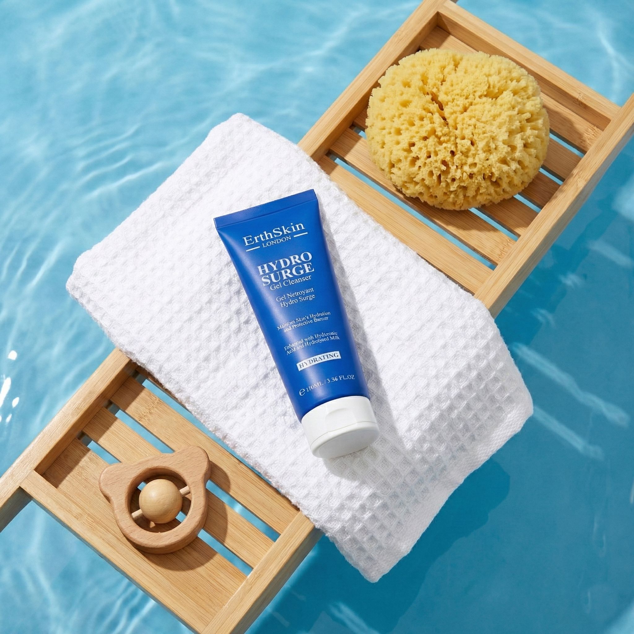 Blaue Tube mit Text. Auf weißem Handtuch, Holztablett mit Schwamm und Spielzeug. Wasserhintergrund.
