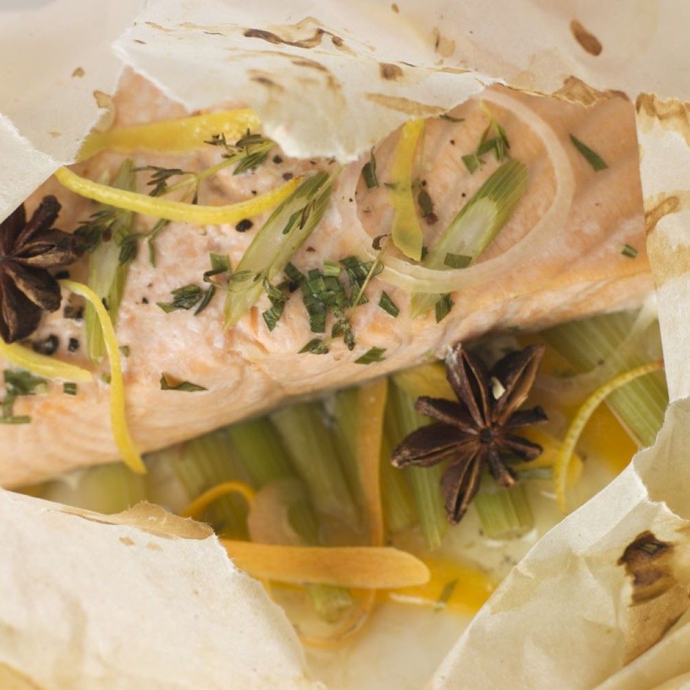 Lachsfilet in Pergamentpapier mit Sternanis, Zitronenscheiben und Kräutern. Nahaufnahme.
