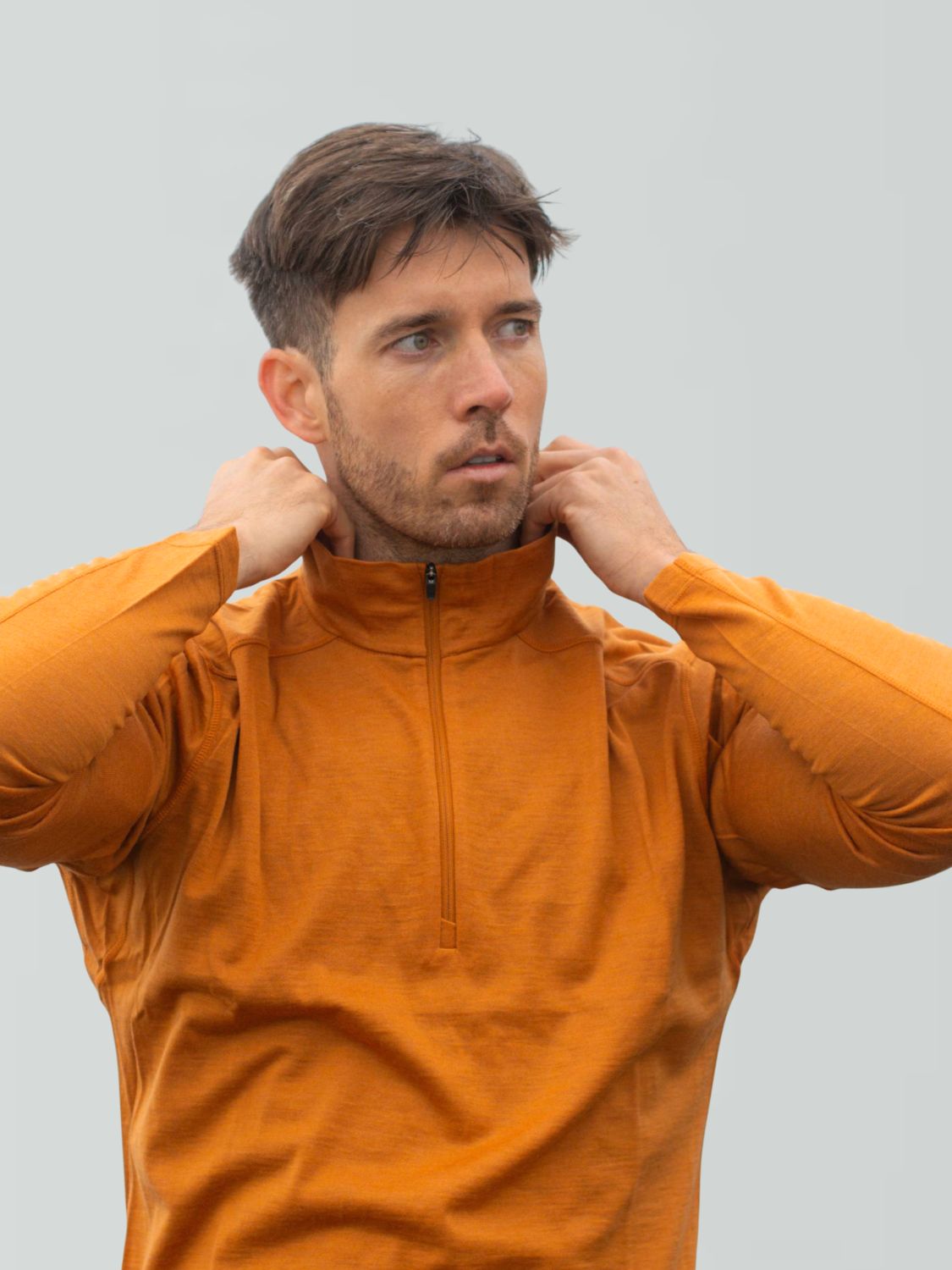 Mann passt den Kragen seines orangefarbenen Merino-Pullovers mit Reißverschluss an.