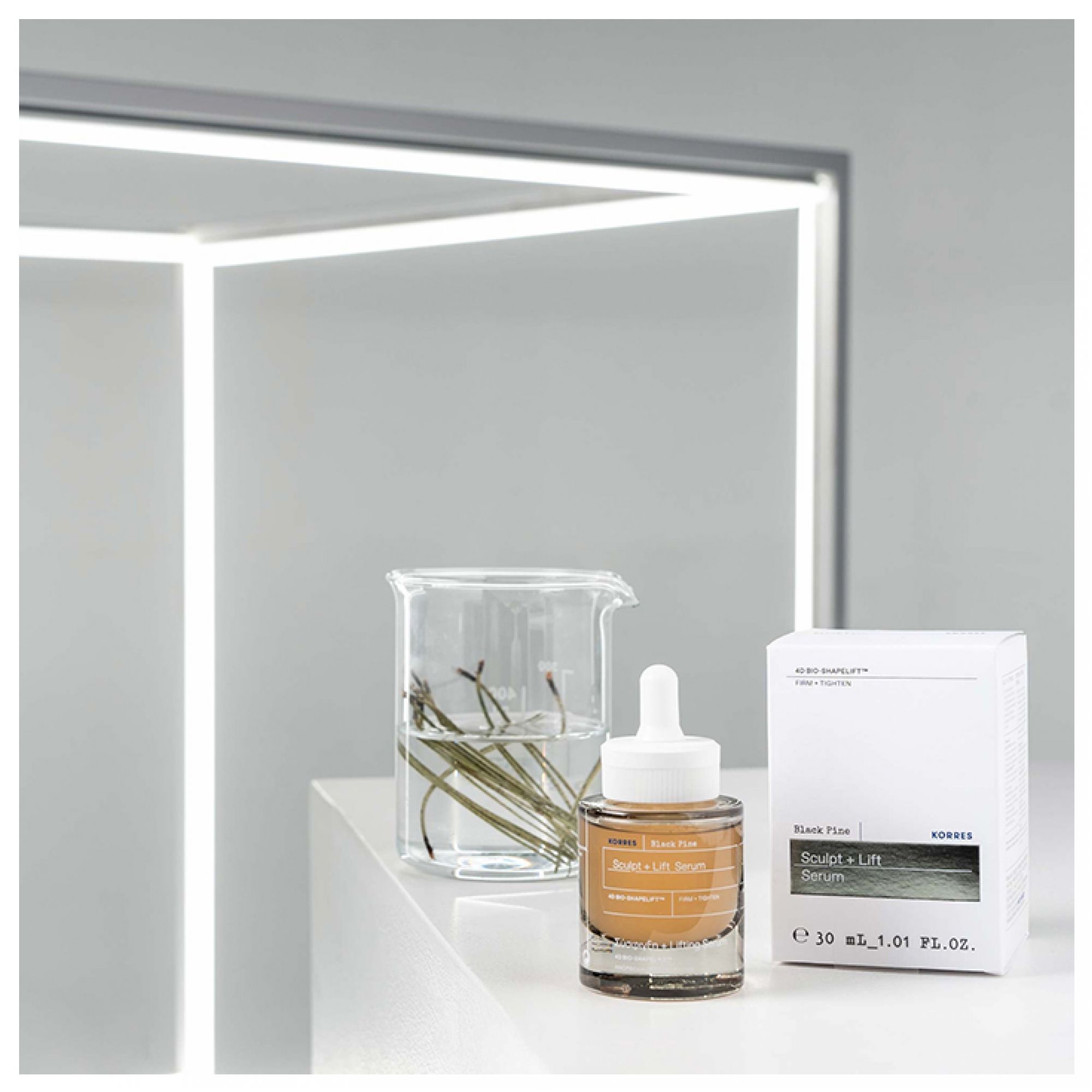 Korres Black Pine Sculpt + Lift Serum Flasche und Verpackung neben Becherglas.