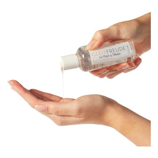 Hand gießt klares Gel aus einer Flasche mit weißem Deckel. Aufschrift: GLEITFREUDE, Anal Gleitgel auf Silikonbasis. 100ml.