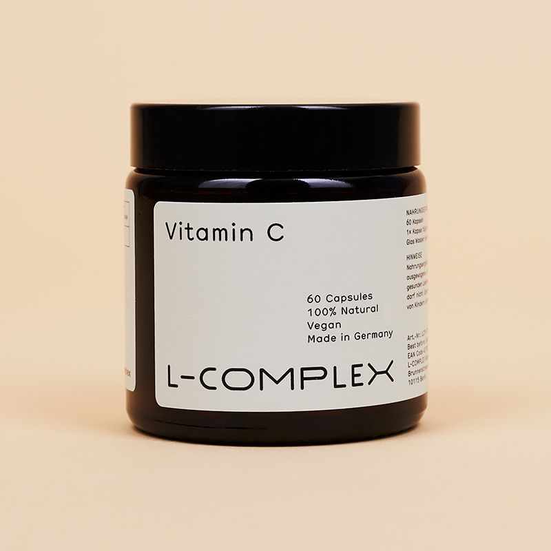 Schwarzes Glas mit Vitamin C Kapseln. Aufschrift: L-COMPLEX, 60 Kapseln, 100% Natural, Vegan.