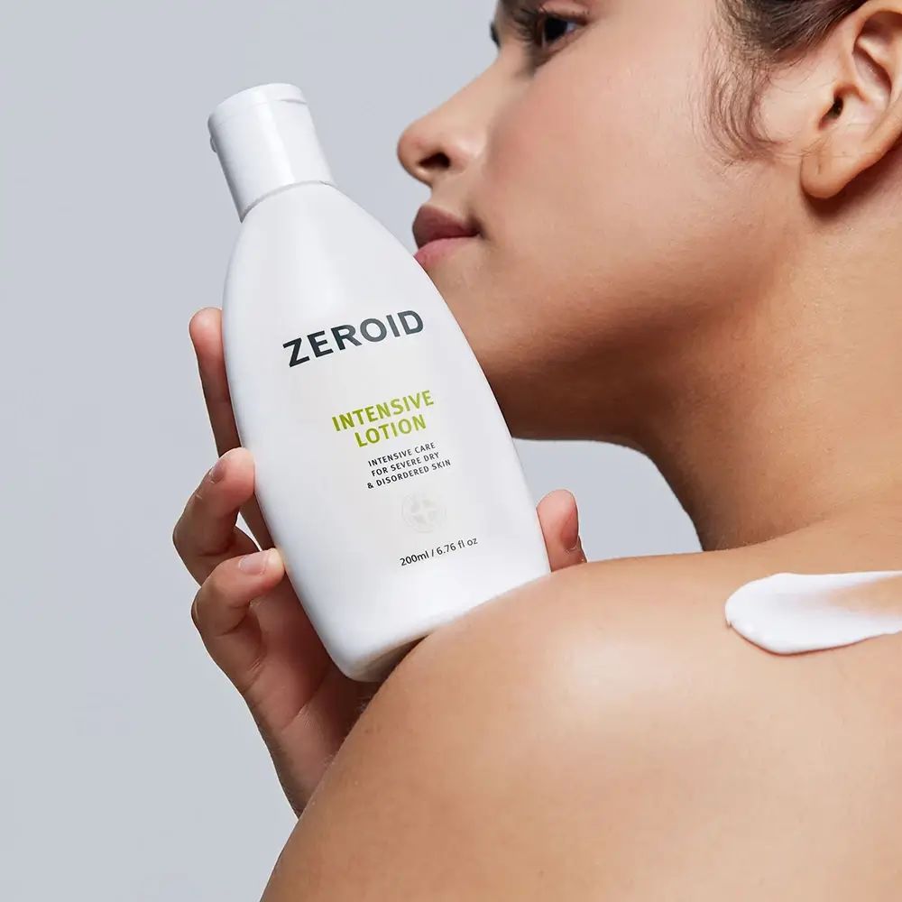 Person hält ZEROID Intensive Lotion Flasche. Creme auf Schulter aufgetragen. Grüner Text.
