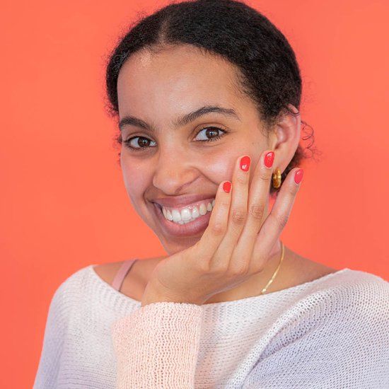Frau mit rotem Nagellack auf den Fingern. Sie lächelt und hält die Hand ans Gesicht.