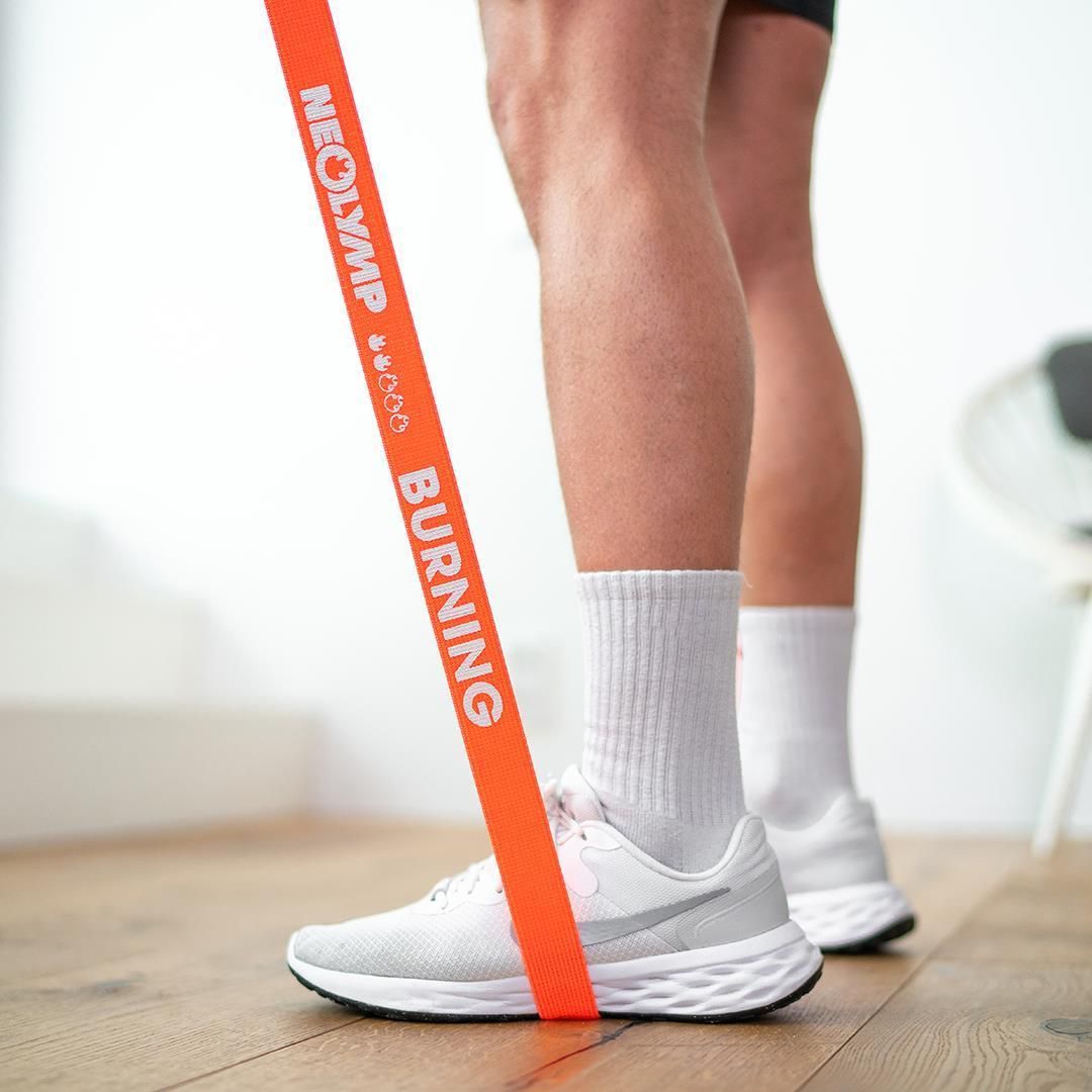 Mann mit Fitnessband am Fuß. Band orange, Aufschrift: BURNING, NEOLYMP.