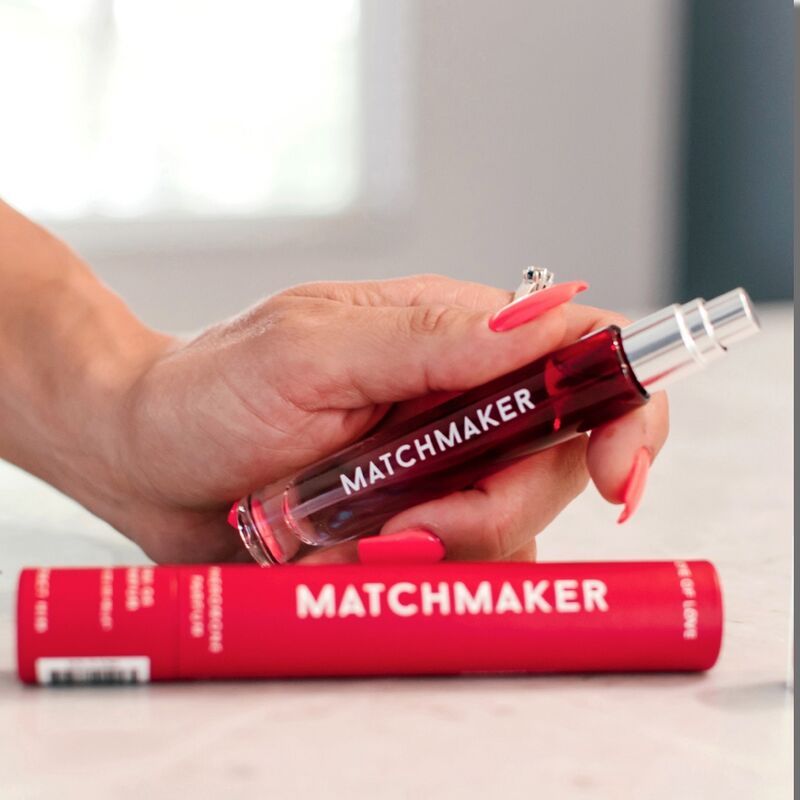 Person hält eine rote Parfümflasche "MATCHMAKER" und die Verpackung. Rote Nägel.