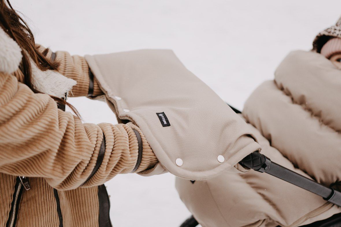 Beige Kinderwagen-Handwärmer aus Stoff mit Druckknöpfen und einem kleinen schwarzen Etikett.