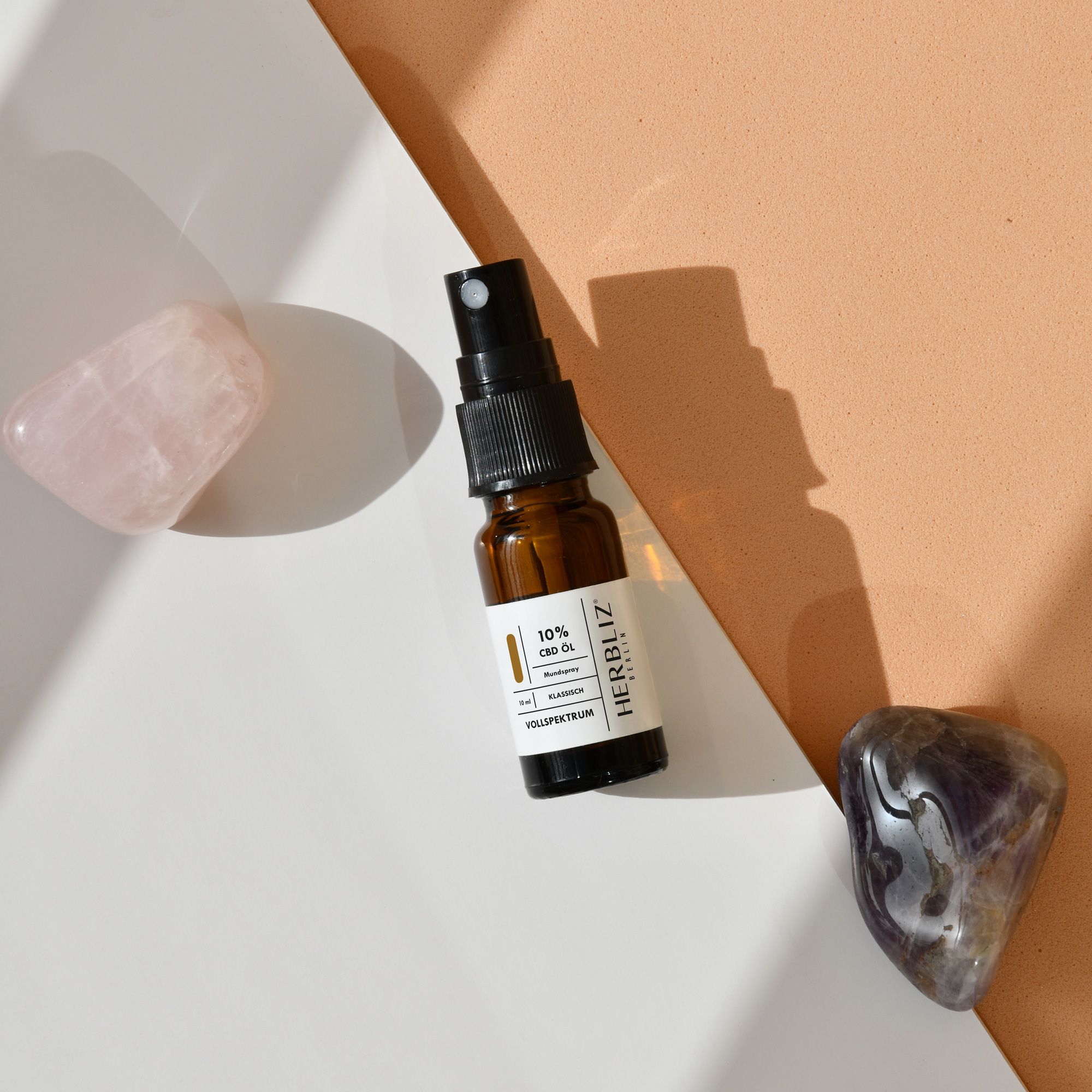 Braune Glasflasche mit schwarzem Sprühkopf, neben Rosenquarz und Amethyst. Aufschrift: 10% CBD.