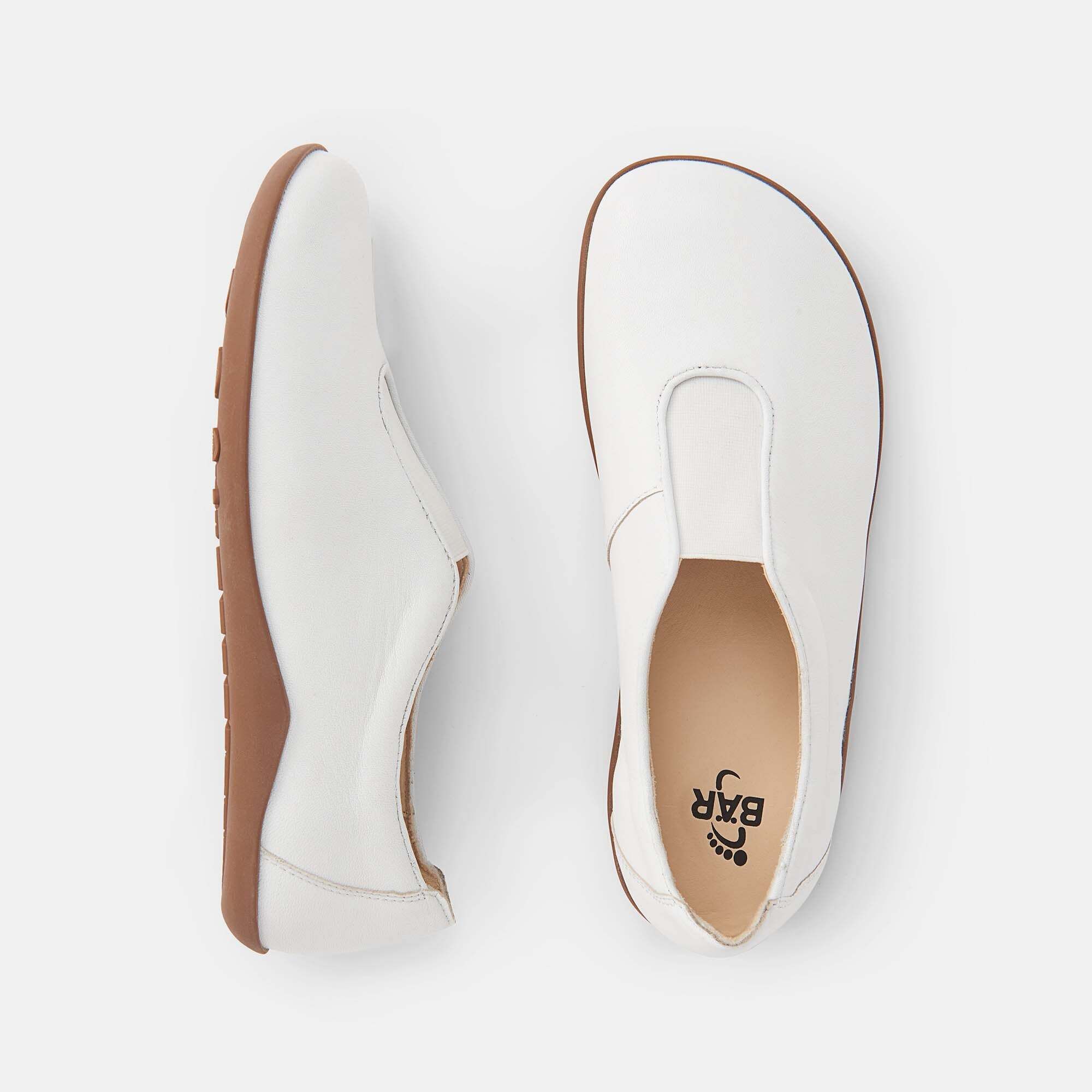 Oberansicht von zwei weißen Damen-Slippern aus Leder mit brauner Sohle. Ein Schuh zeigt das BÄR-Logo.