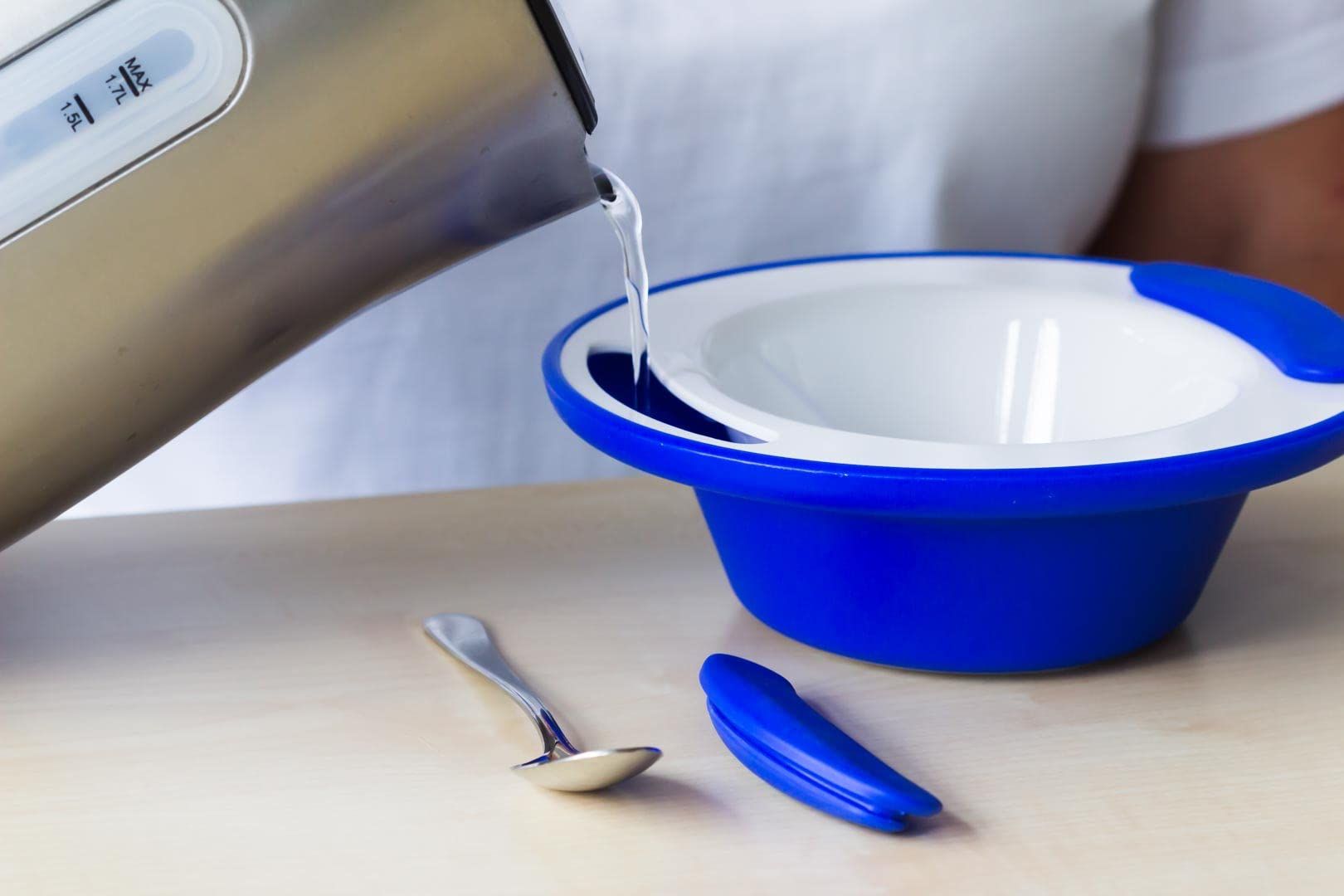 Blaue Thermoschale, Wasser wird eingefüllt. Edelstahl-Wasserkocher. Löffel liegt daneben. Blaue Griffe.