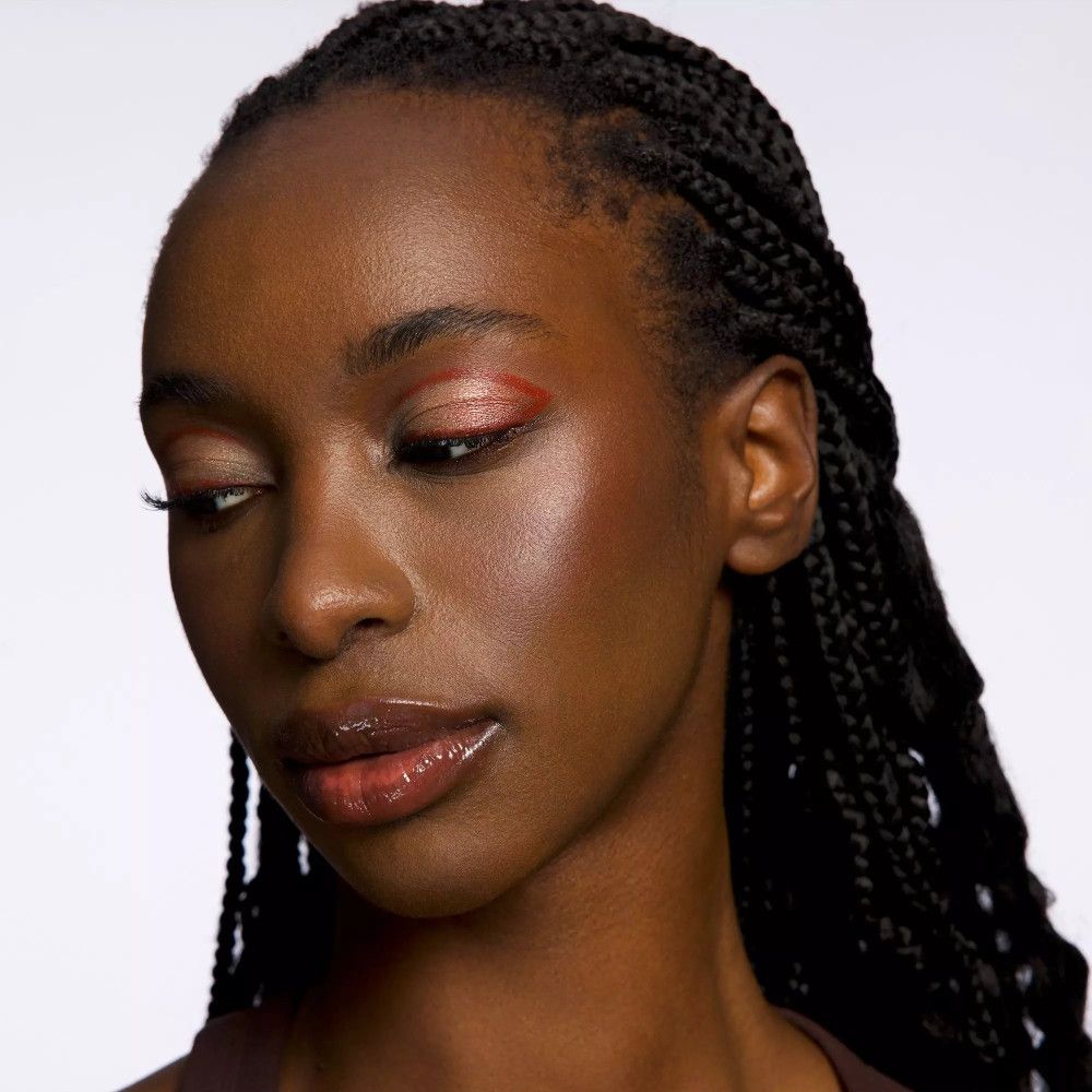 Nahaufnahme einer Frau mit geschminkten Augen und Wangen. Warme Farbtöne. Dunkle Haut, geflochtene Haare.