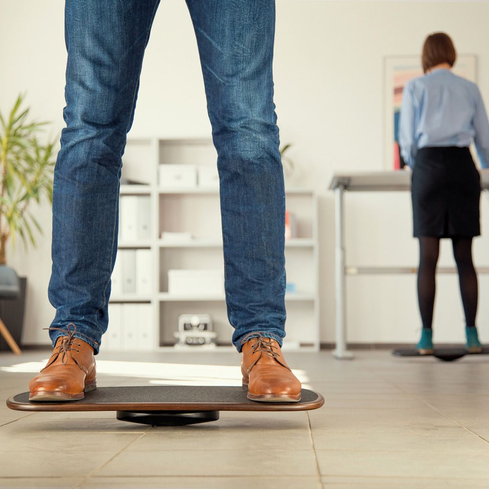 Zwei Personen stehen auf Balanceboards. Nahaufnahme der Füße und Boards. Büro-Hintergrund mit Schreibtisch.