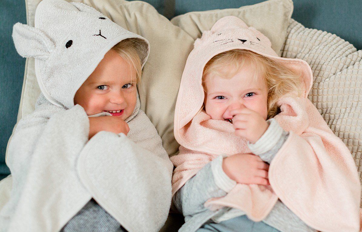 Zwei Kinder in Kapuzenhandtüchern. Eines grau mit Hasenohren, das andere rosa.