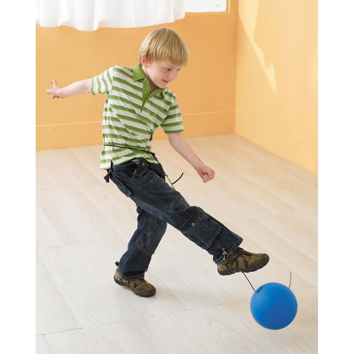 Kind tritt blauen Ball. Ball an Schnur. Kind trägt Jeans und gestreiftes Hemd.