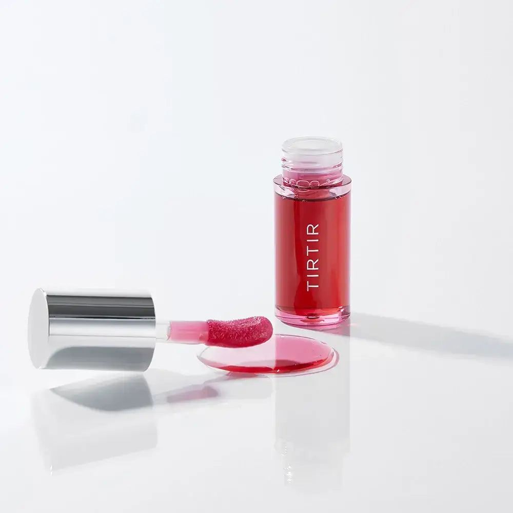 Lip Oil mit roter Flüssigkeit und silbernem Deckel. Der Applikator liegt daneben. Flüssigkeit ist verschüttet.