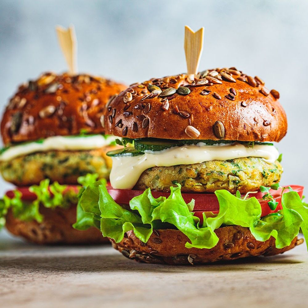 Zwei Falafel-Burger mit Salat, Tomaten und Sauce. Brötchen mit Samen. Holzspieße.