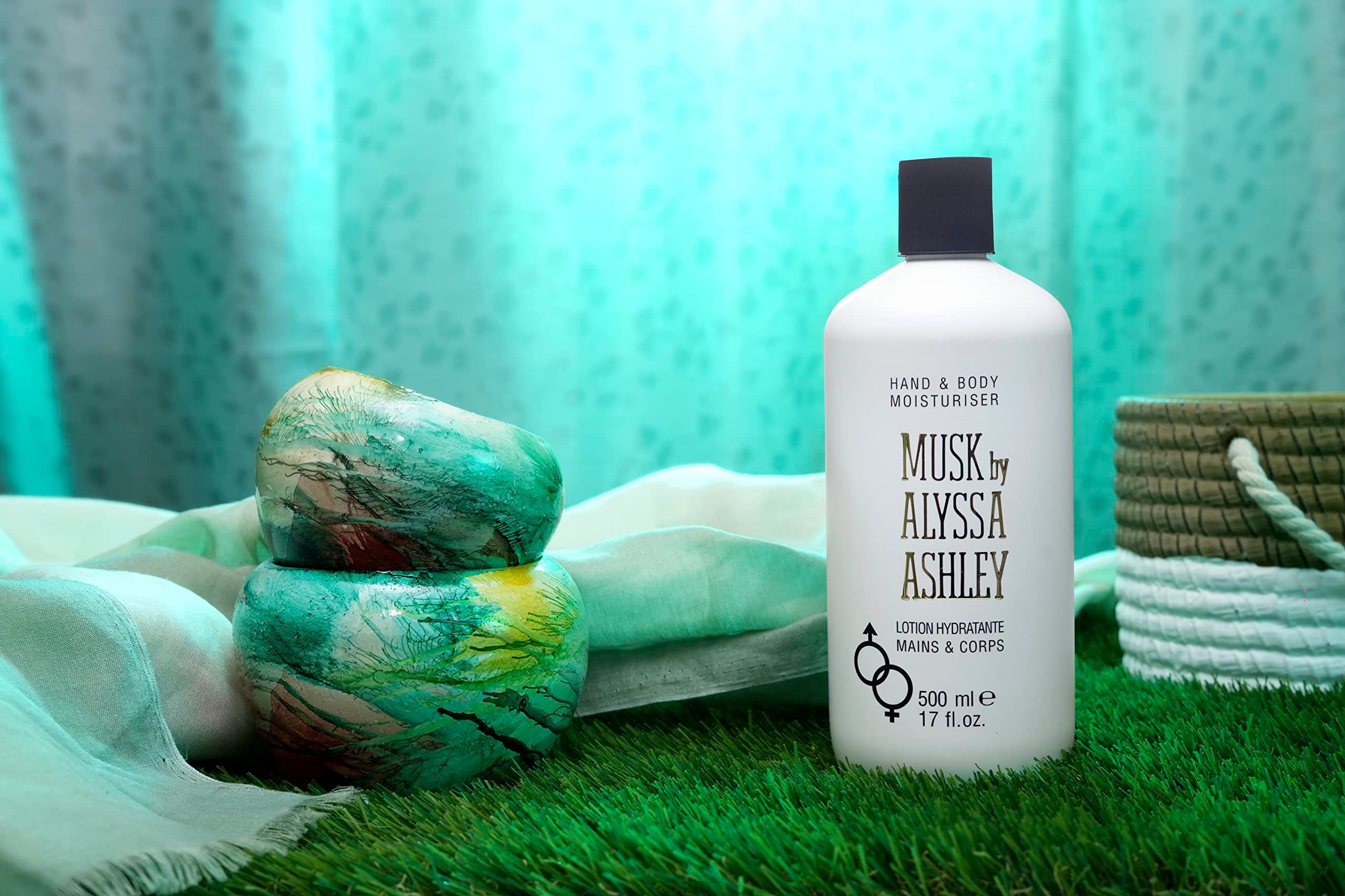 Weiße Flasche mit schwarzem Deckel. Aufschrift: Musk by Alyssa Ashley, Hand & Body Moisturiser. Auf Rasen platziert.