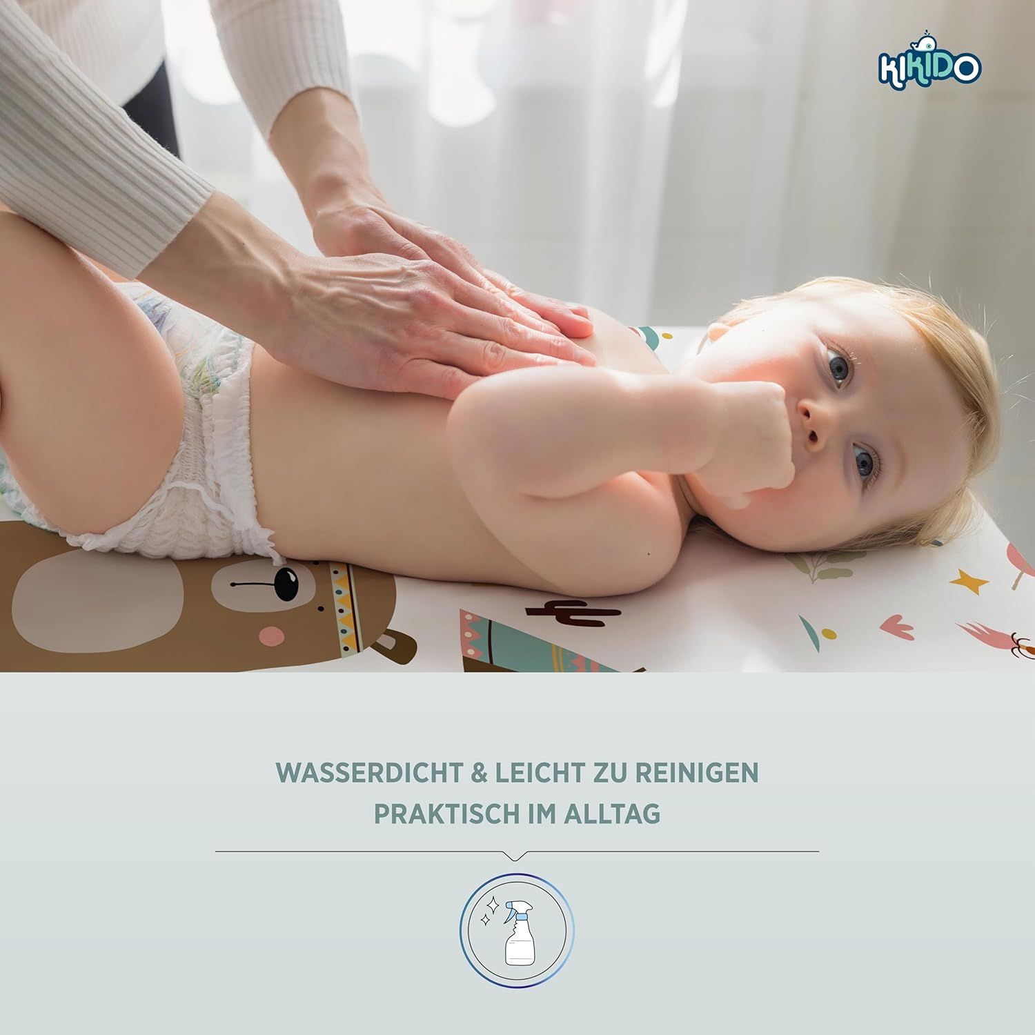 Baby liegt auf Wickelauflage. Hände berühren den Bauch des Babys. Text: Wasserdicht & leicht zu reinigen.
