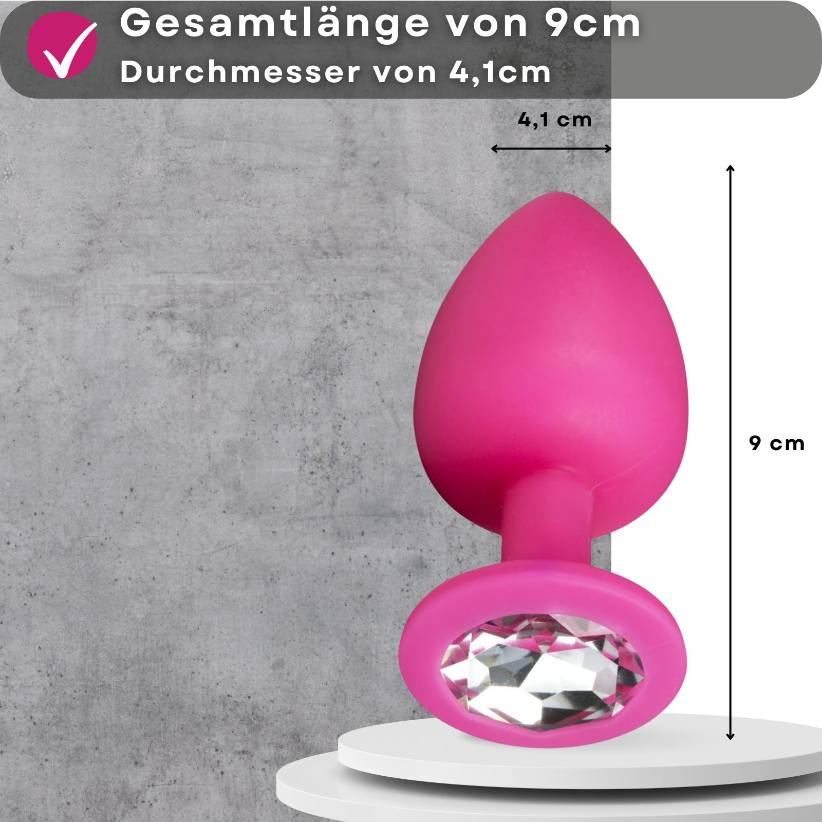 Pinkfarbener Analplug mit Zierstein. 9 cm lang, 4,1 cm Durchmesser. Grauer Hintergrund.