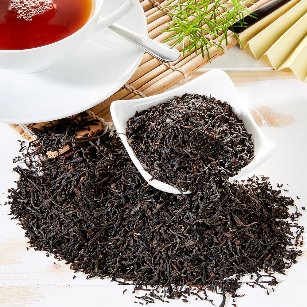 Schwarzer Tee Ceylon OP, lose Blätter in Schale und auf Tisch. Tasse Tee, Löffel, Bambusmatte und Dekoration.