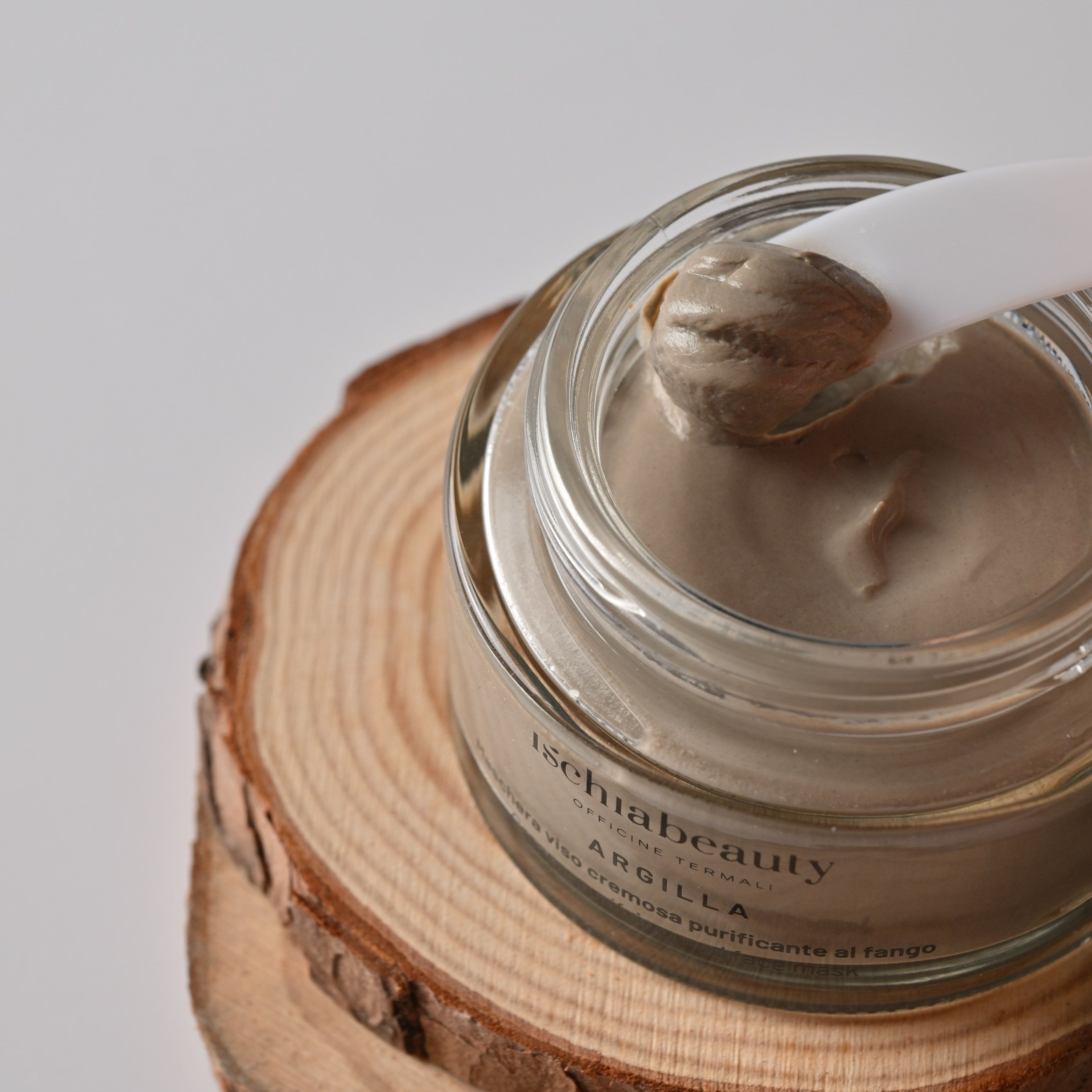 Glas mit Gesichtsmaske, Löffel. Aufschrift: ischiabeauty, ARGILLA, Maschera viso cremosa purificante al fango.