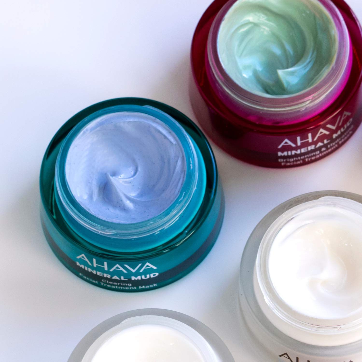 Geöffnete Ahava Mineral Mud Masken. Türkis, blau, weiß. Produktnamen sichtbar. Verschiedene Texturen.