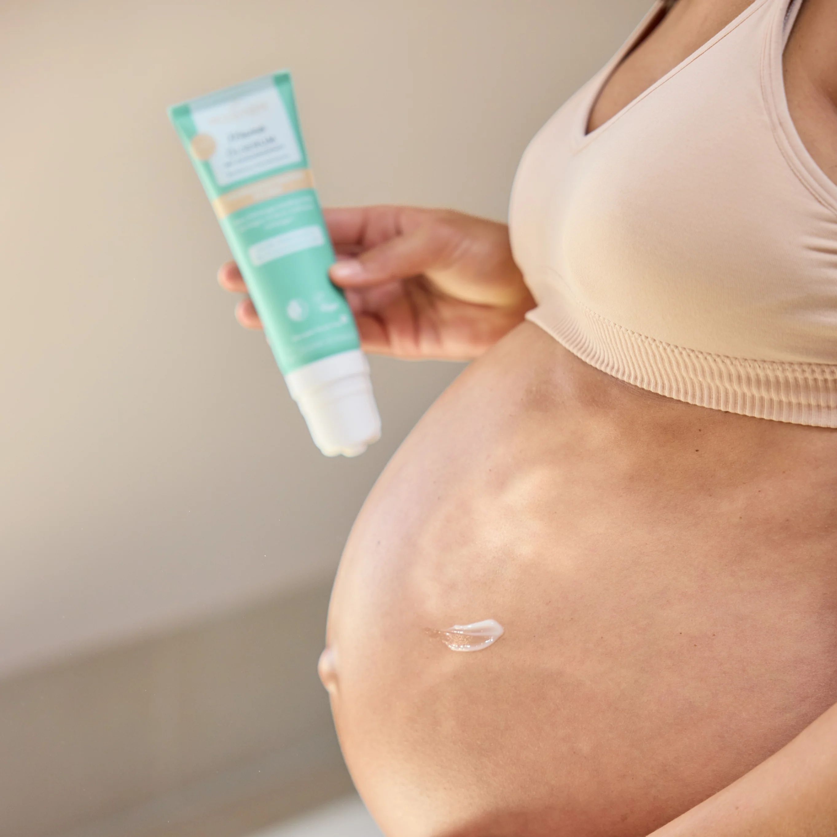 Schwangere Frau hält Tube. Creme auf dem Bauch. Türkis-weiße Tube.