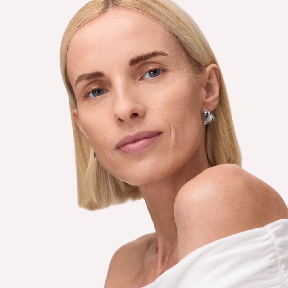 Porträt einer Frau mit blonden Haaren und silbernen Ohrringen. Blick in die Kamera. Helle Haut.