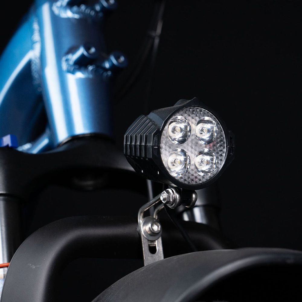 Nahaufnahme des Frontscheinwerfers eines blauen E-Bikes. Vier LED-Leuchten in einem schwarzen Gehäuse.