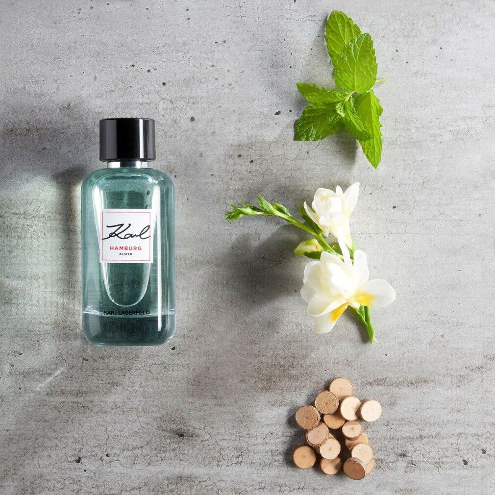 Karl Lagerfeld Hamburg Alster E.d.T. Nat. Spray. Flakon mit schwarzem Deckel, neben Blumen und Holzstücken.