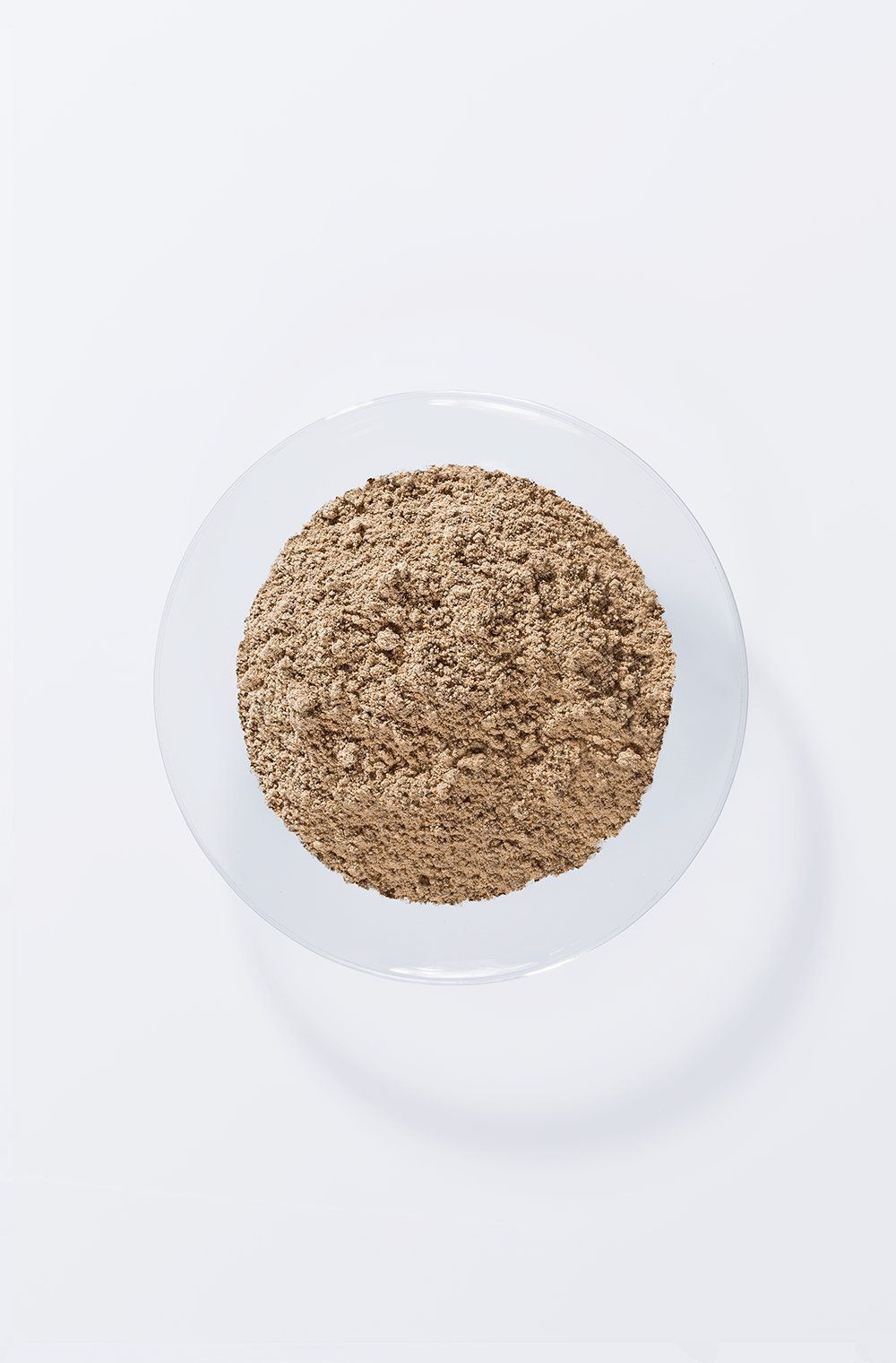 Braunes Pulver in einer transparenten Schale. Draufsicht auf weißem Hintergrund.