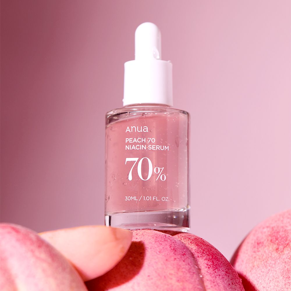 Anua Peach 70 Niacin Serumflasche auf Pfirsichen, rosa Hintergrund.