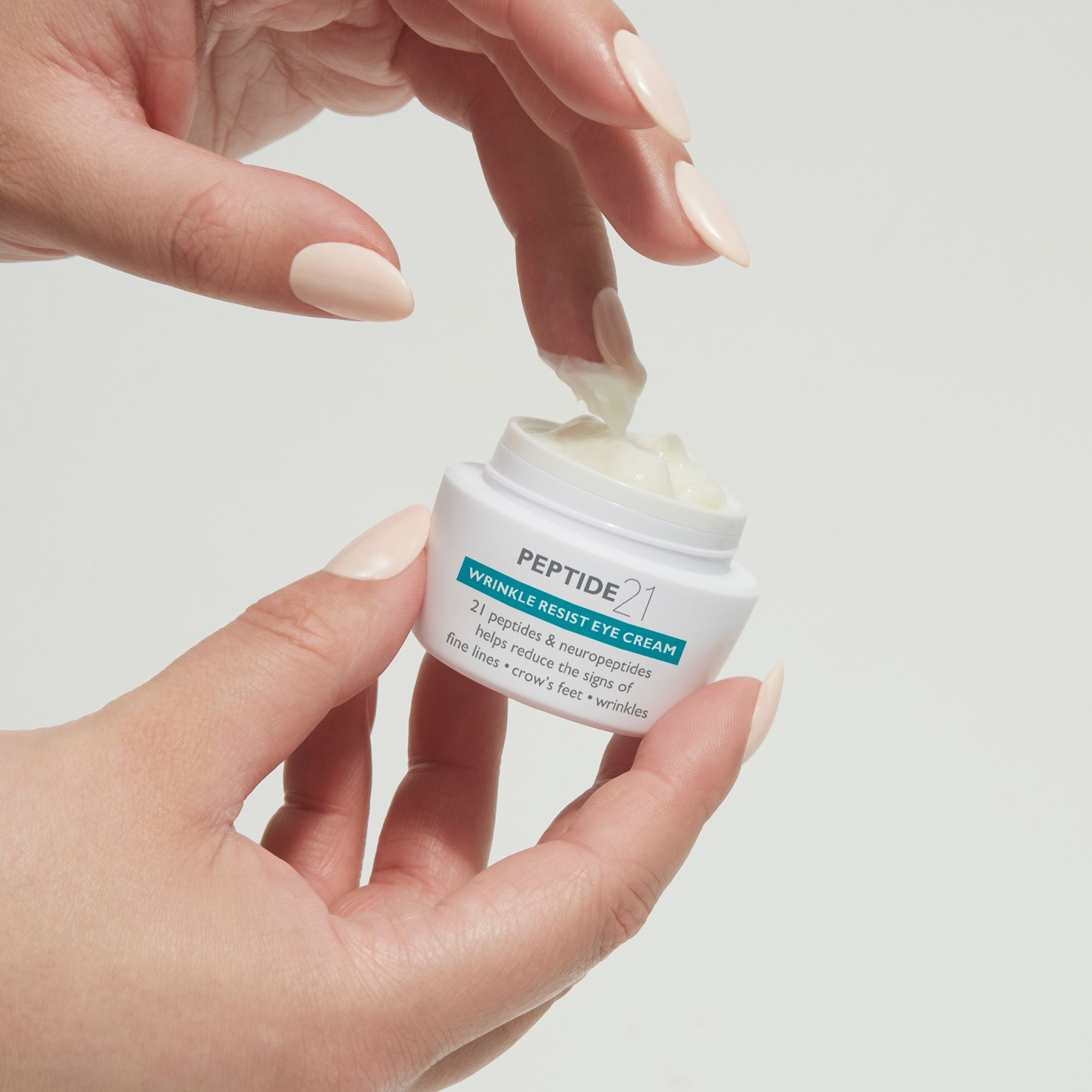 Hände halten Peter Thomas Roth Peptide 21® Wrinkle Resist Eye Cream. Creme wird entnommen.
