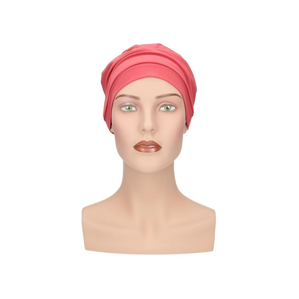 Korallenfarbener Turban auf einer Büste. Mehrere Stofflagen, vorne gerafft. Auf hellem Hintergrund.