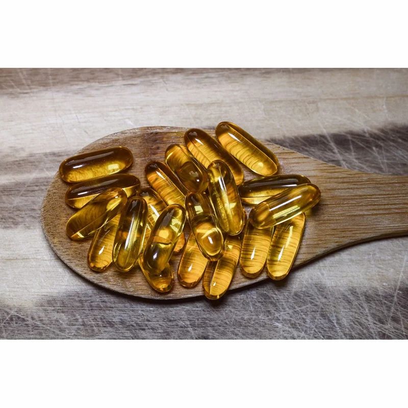 Holzlöffel mit zahlreichen gelben Kapseln. Kapseln sind durchsichtig und länglich. Hintergrund: Holzbrett mit Maserung.