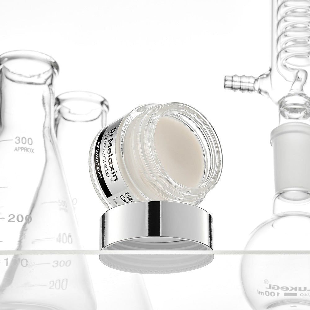 Dr. Melaxin Pigment Corrector Concentrate in einem Glasbehälter mit silbernem Deckel, umgeben von Laborgeräten.